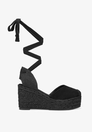 Sandalia de cuña espadrille negra con un tacón de tejido texturizado y un diseño de tiras cruzadas. Fabricada con material de ante.