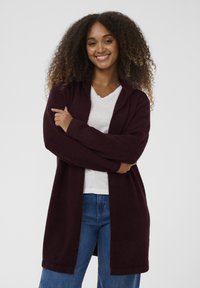 Bordo odprt kardigan, mehka tekstura, dolgi rokavi in sproščen kroj. Kombiniran z belo majico z V-izrezom in modrimi jeans hlačami.