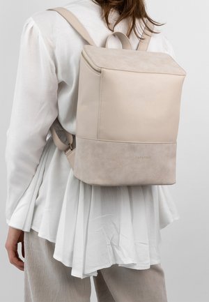 Zaino beige in pelle con texture lisce e scamosciate, caratterizzato da una forma squadrata, cerniera superiore e scritta dorata alla base.