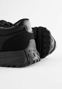 Czarne sportowe buty z teksturowaną cholewką z zamszu i siateczki, wyściełanym kołnierzem oraz masywną gumową podeszwą z wyraźnym wzorem przyczepności.