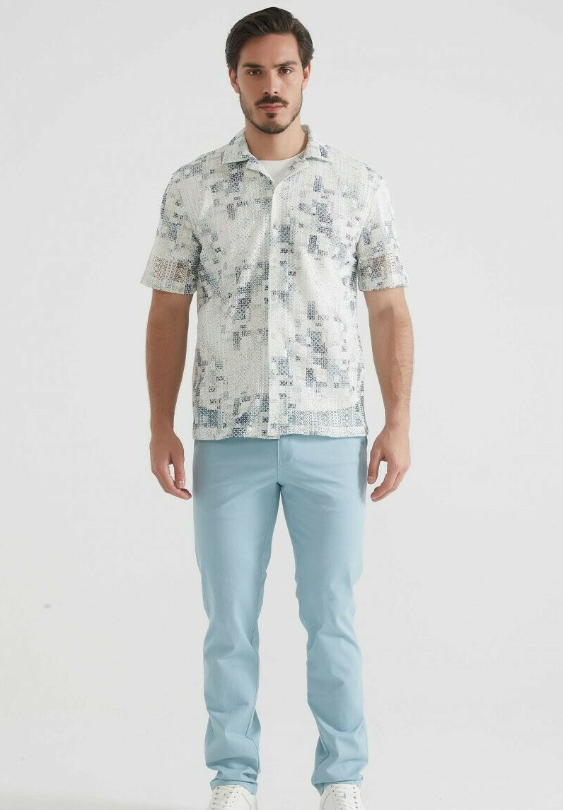 Chemise à manches courtes à boutons de couleur crème avec un motif géométrique bleu ; associée à un pantalon bleu clair et des baskets blanches.