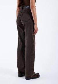 Weite dunkelbraune Jeans aus Denim mit einer glatten Textur. Verfügt über zwei Gesäßtaschen und ein Etikett mit dem Markennamen am Bund.