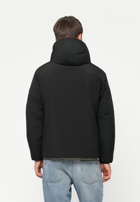 Black puffer jacket with a high collar, smooth texture, and a relaxed fit. The back features a slightly rounded hem and minimal detailing.