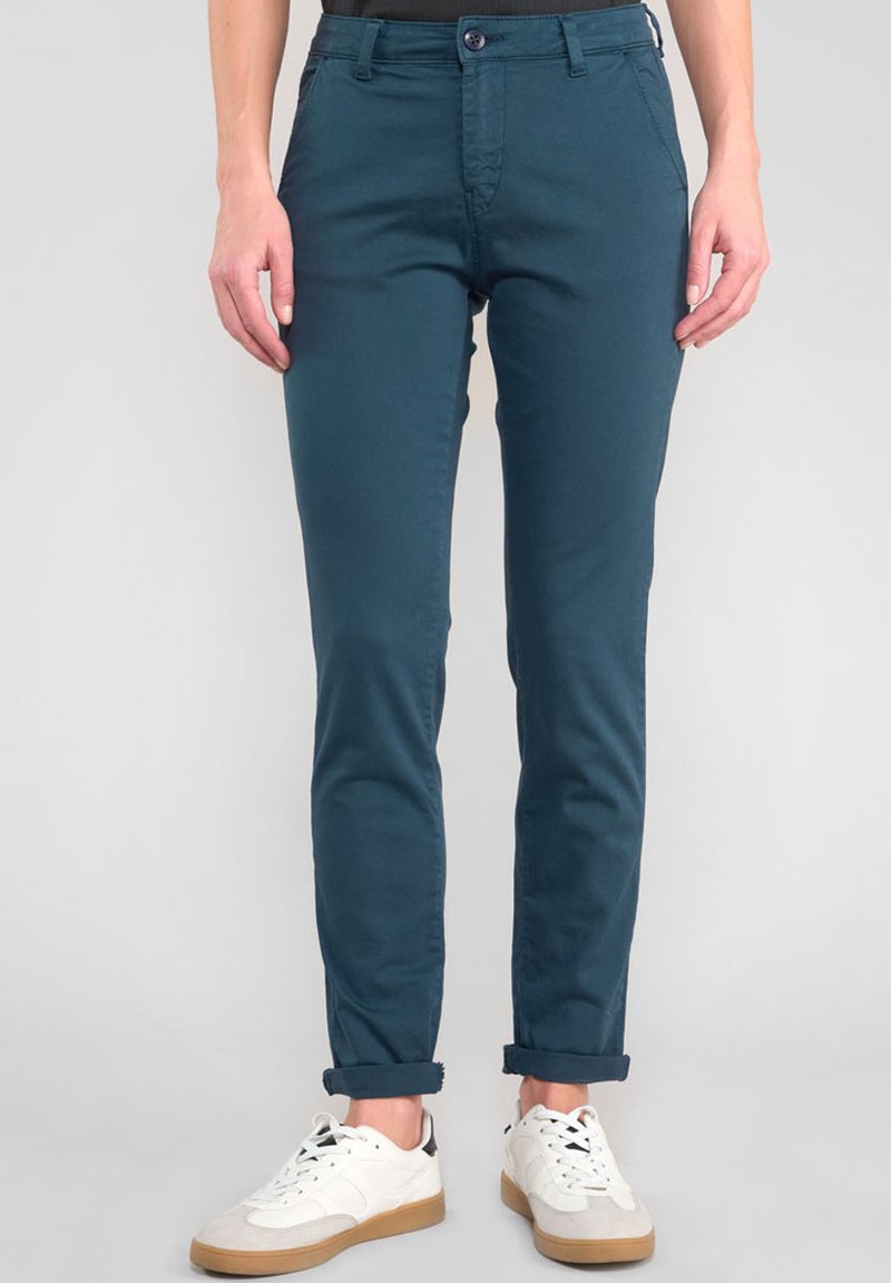 Pantalons ajustés teal en mélange de coton, avec un design classique à cinq poches, fermeture à bouton et ourlets retroussés, associés à des baskets blanches.