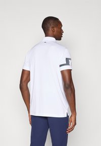 Hvit polo skjorte med korte ermer, med et mønstret akcent på venstre erme. Myk stoff og sidespalter i kanten for komfort.