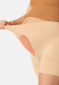 Pantaloni corti beige elasticizzati con una superficie liscia, caratterizzati da un design a forma di cuore arancione in contrasto. Lunghezza a metà coscia con una vita alta.
