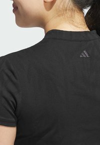Crna sportska majica s teksturiranim uzorkom, kratkim rukavima i malim reflektirajućim Adidas logotipom na leđima blizu izreza.