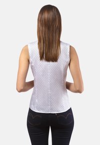 Blusa bianca senza maniche con un sottile motivo blu, texture liscia e orlo arrotondato. Abbinata a jeans in denim scuri.
