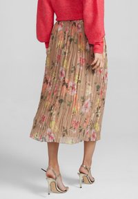 Rok midi berlipat berwarna cokelat dengan motif floral dalam warna merah muda, oranye, dan hijau. Dipadukan dengan sweater koral dan sandal hak tinggi metalik.