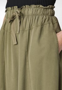 Fustă din material ușor, de culoare verde măsliniu, cu talie elastică și șnur ajustabil. Prezintă buzunare laterale și un design lejer.