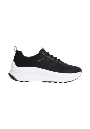 Baskets de sport Calvin Klein noires avec semelle épaisse blanche, dessus en tissu, lacets noirs, et languettes de traction au talon et à la langue.