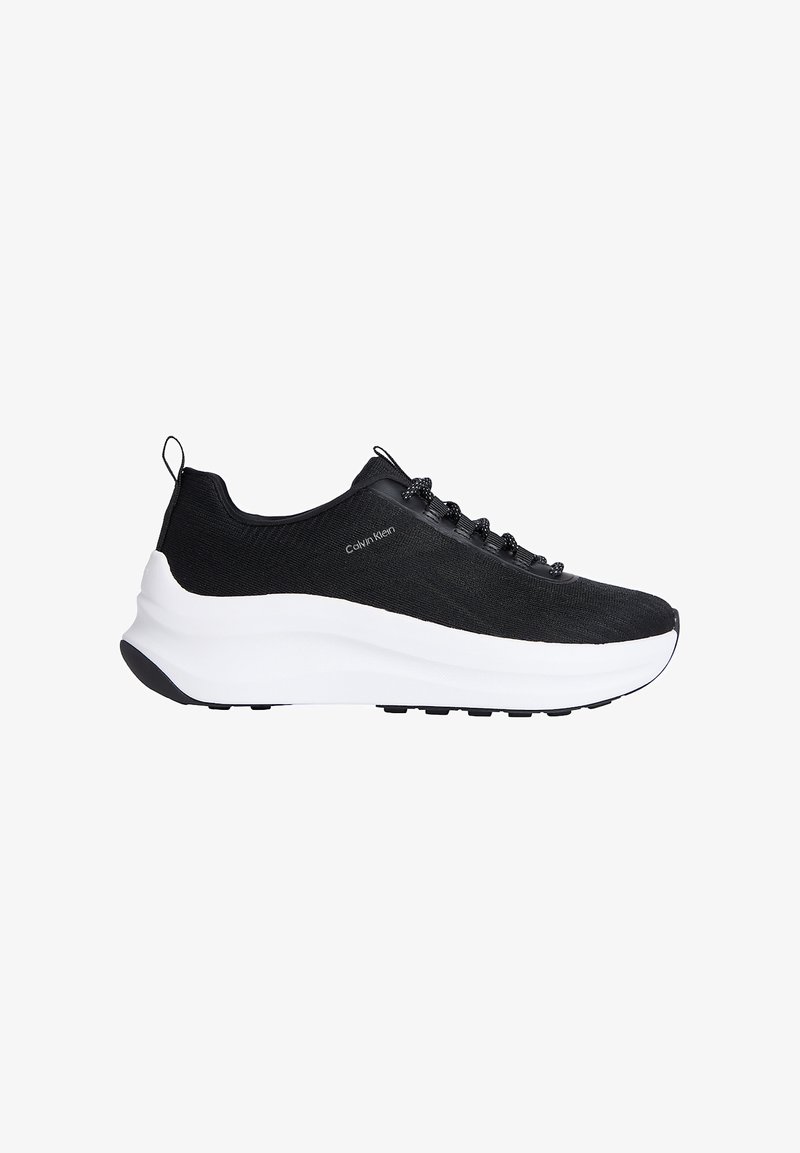 Baskets de sport Calvin Klein noires avec semelle épaisse blanche, dessus en tissu, lacets noirs, et languettes de traction au talon et à la langue.