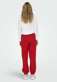 Hvid langærmet skjorte og røde sweatpants med elastiske manchetter. Outfittet har en afslappet pasform og er parret med hvide sneakers.