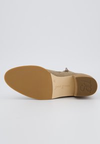 Zapato beige perforado con suela flexible. Cuenta con un tacón bajo y una sutil marca en la plantilla, diseñado para ofrecer comodidad y transpirabilidad.