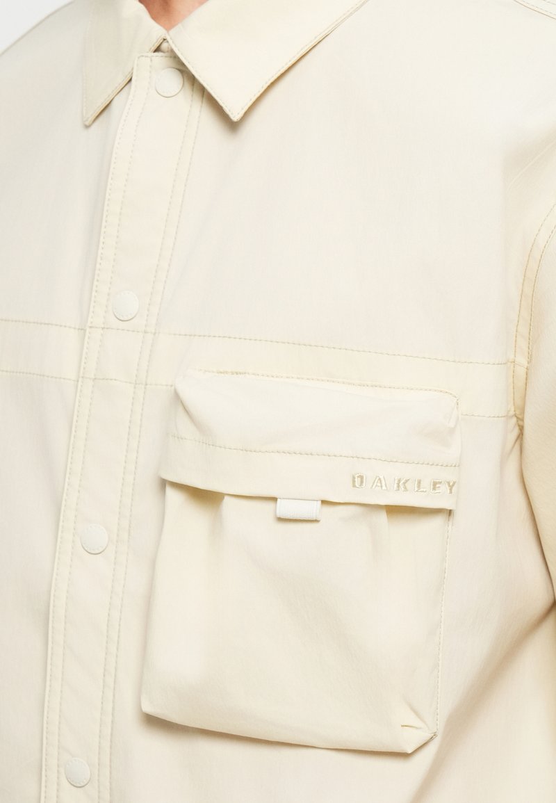 Giacca beige chiaro realizzata in tessuto liscio, con design a bottoni, colletto e tasca frontale con logo del marchio impresso.
