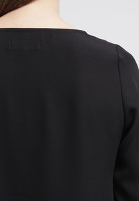 Svart plagg med en slät textur och en vid halsringning. Baksidan har en ren finish med minimal detaljering.
