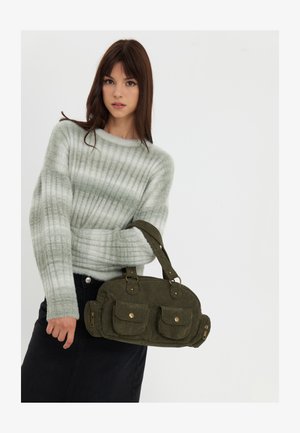 Olijfgroene corduroy handtas met twee voorzakken, gouden hardware en een korte schouderband. Draagt men met een lichtgroene gestreepte trui.