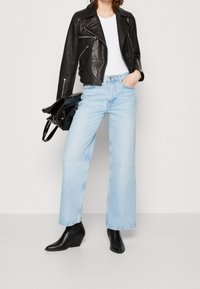 Černá kožená motorkářská bunda, bílý tričko, světle modré široké džíny a černé klokankové kotníkové boty, spolu s černou kabelkou.