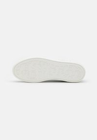 Biała podeszwa sneakersów z teksturowanej gumy. Logo "GUESS" wytłoczone wielokrotnie w całości. Gładkie krawędzie, minimalistyczny design, brak widocznych akcentów.