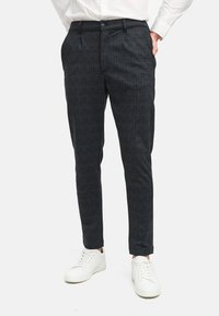 Slim-fit donkergrijze geruite broek met een lichte textuur, subtiele patronen en zijzakken, gecombineerd met witte sneakers.