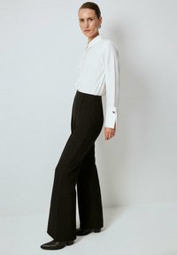 White collared shirt with long sleeves, paired with fitted black flared trousers. Black ankle boots and silver earrings add detail.