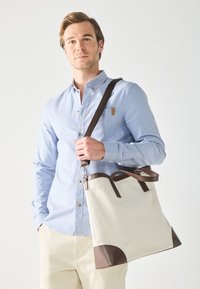 Canvas tote bag in off-white with brown leather accents, featuring dual top handles and a detachable shoulder strap. Smooth, structured design.