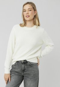 Un pull en tricot blanc et duveteux avec un col rond et des poignets côtelés, associé à un jean gris au design classique à cinq poches.