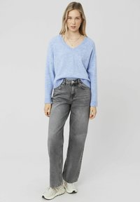 Un pull tricoté bleu clair avec un col en V et des poignets côtelés, associé à un jean large gris taille haute et des baskets blanches.