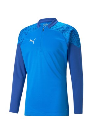 Langarm kwart-rits trui in het blauw met een textuurpatroon in geometrische vormen op de schouders, met een wit logo op de borst.