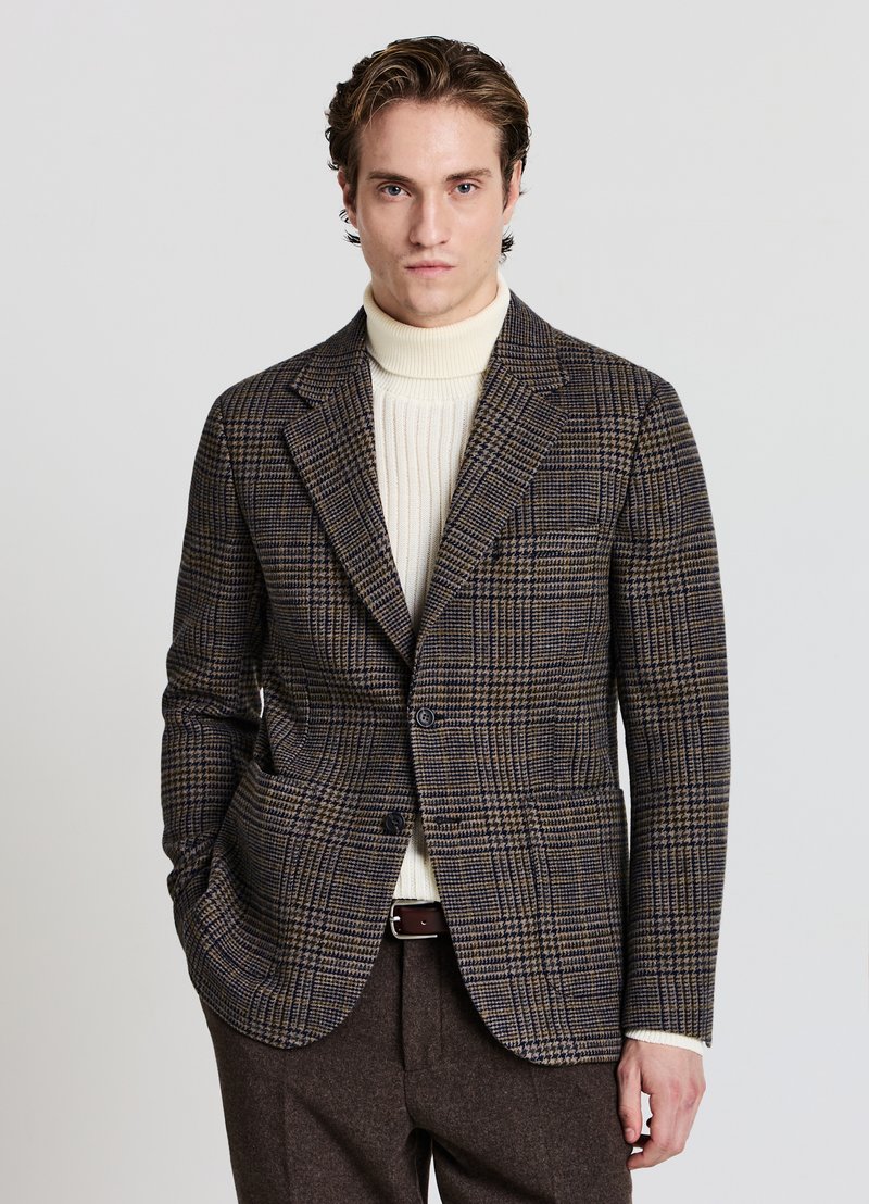 Blazer a scacchi marrone e blu realizzato in tessuto testurizzato, con chiusura a singolo bottone e due tasche laterali, indossato sopra un dolcevita crema.