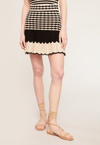 Abito in maglia con motivo a righe in nero e beige, caratterizzato da una gonna svasata e un orlo a onda. Sandali beige con cinturini completano il look.