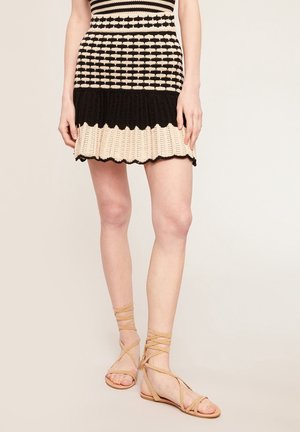 Knit dress with a striped pattern in black and beige, featuring a flared skirt and scalloped hem. Strappy beige sandals complete the look.