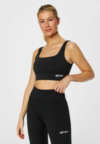 Svart sports-bh og høy midje tights med glatt tekstur. Har firkantet utringning og brodert logo på båndene.
