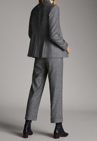 Costume texturé gris avec une veste cintrée et un pantalon ample, associé à des bottines noires. Le tissu présente un motif subtil.