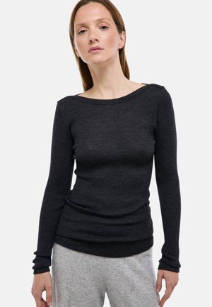 Haut noir côtelé à manches longues avec un large col, une silhouette ajustée et un tissu texturé. Porté avec un pantalon de survêtement de couleur claire.