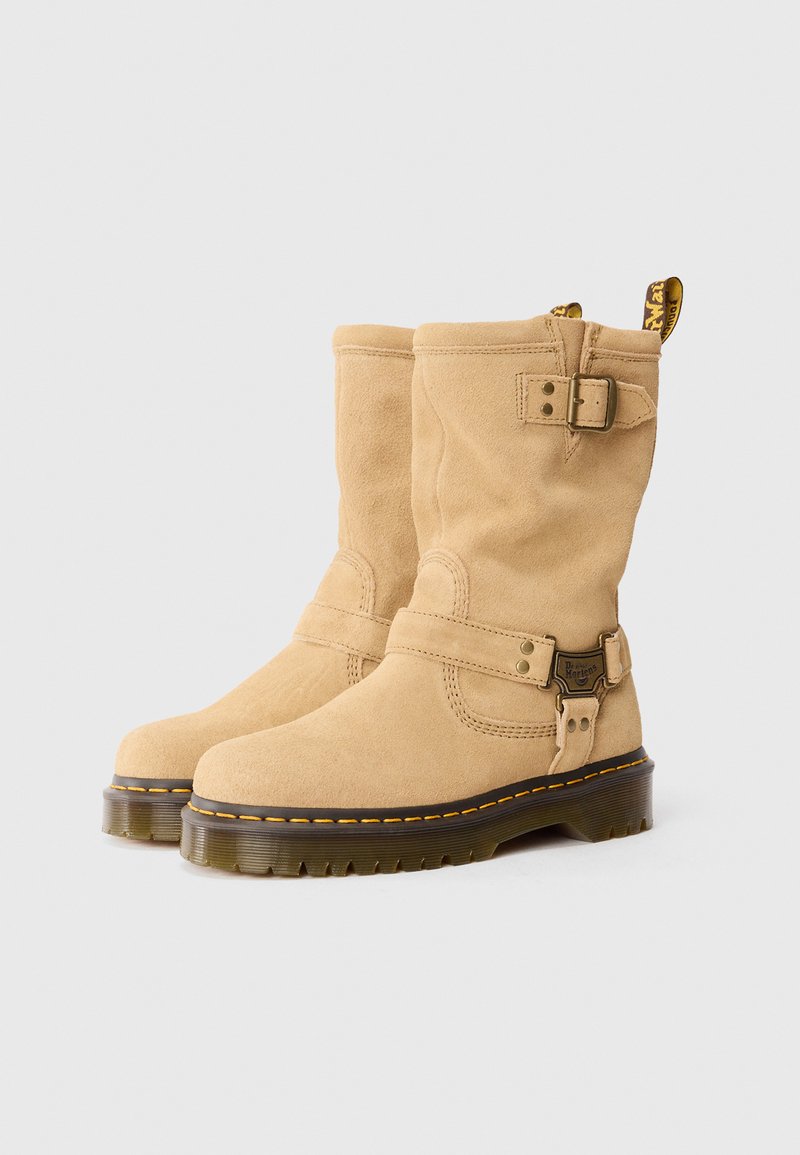 Bottines en daim beige avec une semelle rembourrée, des détails de sangle à boucle et des coutures jaunes le long de la semelle en caoutchouc noir.