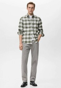 Camisa de botones de cuadros verdes y blancos, de manga larga, combinada con pantalones grises y zapatos negros. Presenta un collar y un bolsillo frontal.