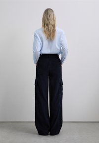Camisa abotonada azul claro combinada con pantalones cargo de pana ancha en un tono azul marino oscuro, con grandes bolsillos laterales y un corte relajado.