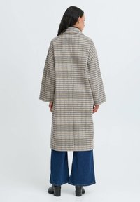Lang, overdimensioneret frakke med et ternet mønster i creme, marineblå og brun, der har en klassisk krave og brede ærmer, parret med flagrende denim jeans.