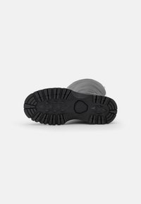 Semelle de botte en caoutchouc noir avec des rainures profondes, motif hexagonal au centre, bords lisses et surface texturée pour plus d'adhérence.