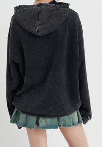 Musta ylipitkä huppari, jossa on teksturoitu pinta ja nyörihuppu, yhdistettynä kerrokselliseen farkkuhameeseen, jossa on revitty helma.