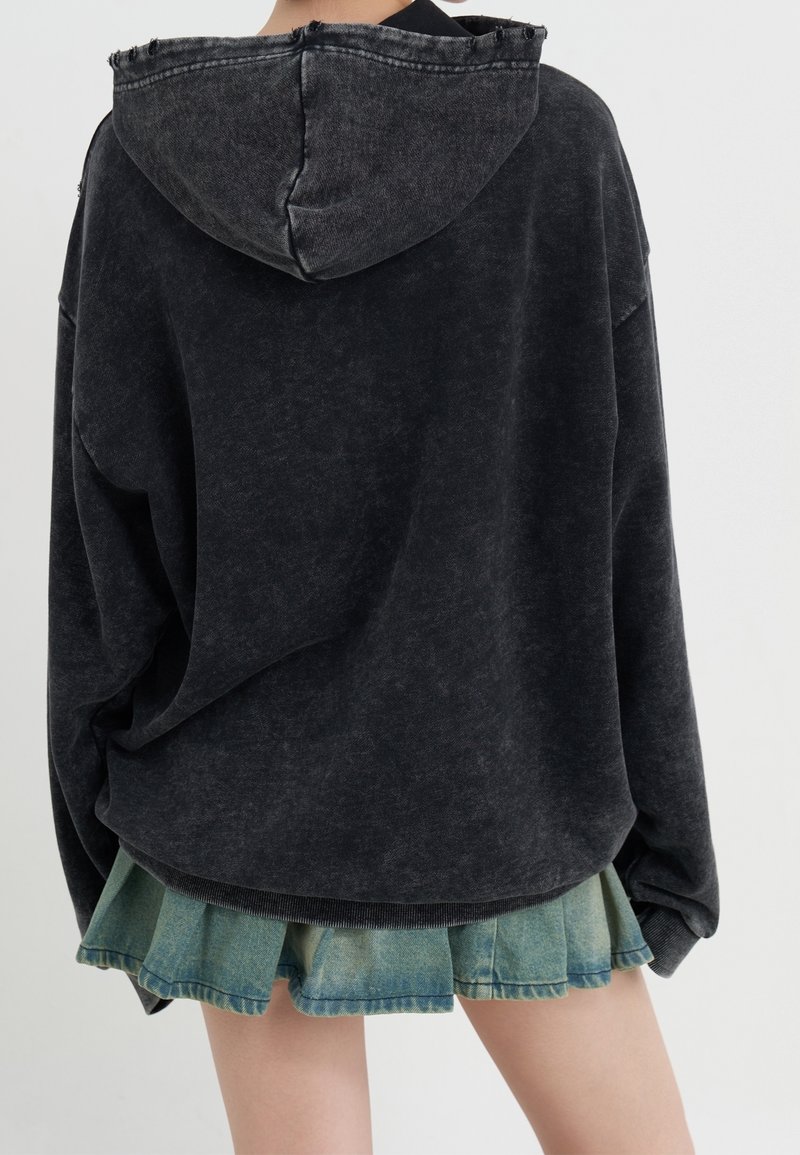 Musta ylipitkä huppari, jossa on teksturoitu pinta ja nyörihuppu, yhdistettynä kerrokselliseen farkkuhameeseen, jossa on revitty helma.