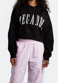 Zwarte cropped hoodie met 'PEGADOS' in witte letters, gecombineerd met lichtroze cargobroek met meerdere zakken en een elastische taille.