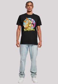 Melnā kokvilnas T-krekls ar krāsainu multfilmu grafiku, kurā attēloti varoņi no "Fleintstoniem". Ikdienas piegriezums ar īsām piedurknēm.