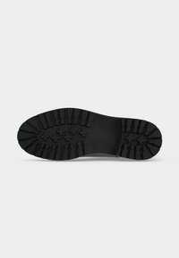 Semelle de chaussure en caoutchouc noir avec des rainures profondes et des motifs en forme de croix pour une meilleure adhérence et durabilité.