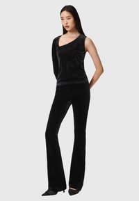 Schwarzes Samt-Ensemble mit einem einseitigen Top und figurnahen, ausgestellten Hosen, das die glatte Textur und die elegante Silhouette betont.