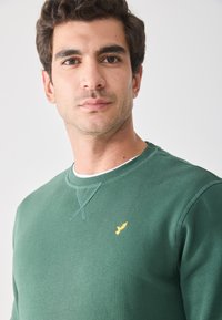 Grüner Baumwoll-Sweatshirt mit Rundhalsausschnitt und gelbem Vogel-Logo. Verfügt über gerippte Bündchen und Kragen. Weiche Textur, lässige Passform.