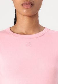 T-shirt ajusté rose avec un col rond, fabriqué en tissu lisse. Présente un logo en relief "HUGO" sur la poitrine.