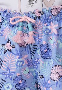Pantalones cortos de pijama de color azul claro con un patrón floral tropical en rosa, verde y azul marino. Presenta una cintura fruncida con un cordón rosa y borlas.