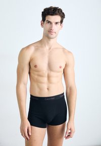 Boxerii negri, confecționați dintr-un material moale, având o talie largă decorată cu "Calvin Klein" în culori contrastante. Modelul este fără cămașă.